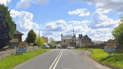 Street view of Rectory Road, in Upper Langwith, Shirebrook, Derbyshire, with signs of the village on either side of the road.