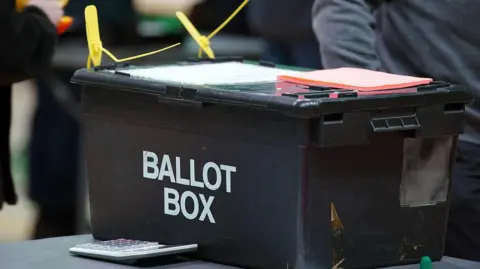 A black container on a table. The words 'ballot box' are written on the side.
