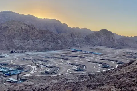 Ben Hoffler A view of one of the developments, still under construction Plain of el-Raha. The sun is behind the surrounding mountains, while the development site is in the foreground, with roads connecting different buildings 