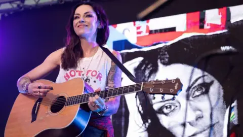 Amy MacDonald with a guitar, tattoos and big smile