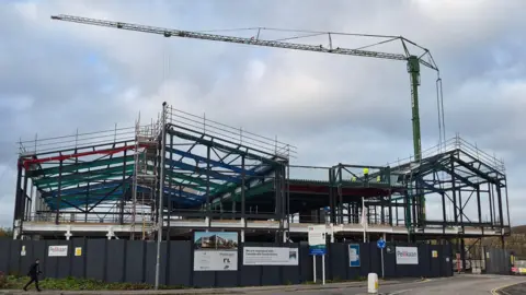 A crane sits behind the shell of a building with large beams