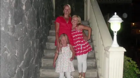 Family handout Julie stands on some steps with her two daughters 