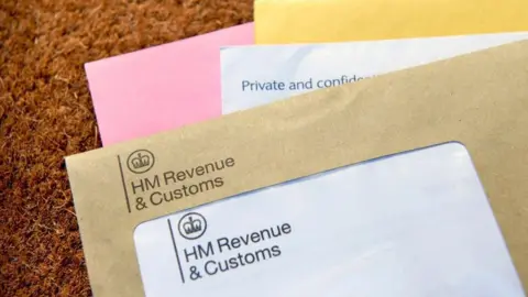 Getty Images Several different colours envelopes on top of each other, yellow, pink, white and brown. The top one has a label saying "HM Revenue and Customs". They sit on an orange carpet.