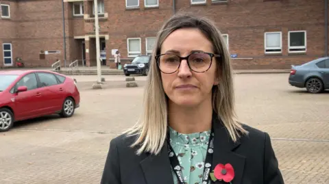 Detective Constable Claire Floyd stood outside Norwich Crown Court. She has shoulder length blonde hair, round glasses and a poppy pinned to a black suit jacket.