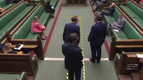 UK Parliament The health secretary steps over yellow-and-black tape - in place to help people to maintain social distancing - to greet another colleague