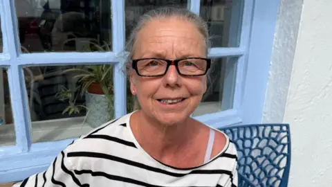Tracey Benn is wearing a white Breton top with black stripes and she is wearing glasses. 