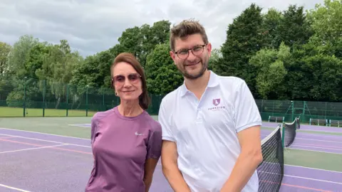 Wendy Hurrell A woman and a man stand at a tennis net smiling