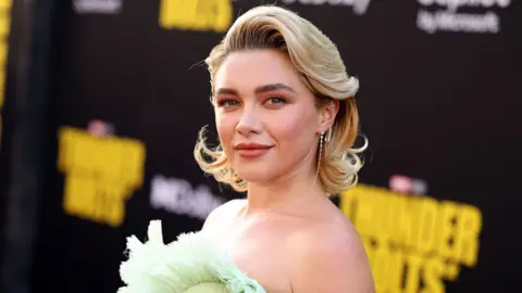 Florence Pugh wearing a green dress on the red carpet in front of a Thunderbolts* sign