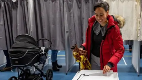 A voter casts her ballot while her baby waits near by in Nuuk, Greenland