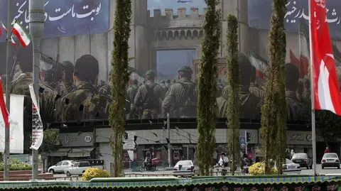 An enormous mural depicting members of the military on the corner of a building in Tehran. Below it, cars drive by on the street.
