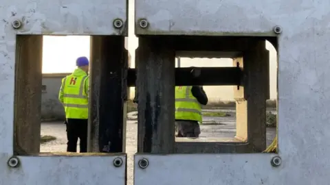 A shot looking through the gates of casement park, showing two workers inside in high-viz jackets