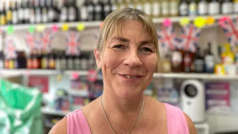 Woman in a pink top and necklace in front of a shop display