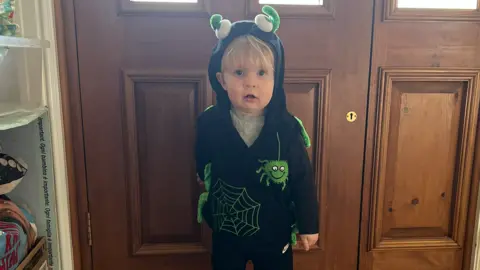 Cillian in front of a wooden front door in a black hoodie, which has a large spider and a large cobweb on it. 