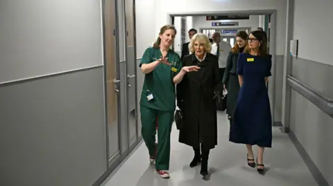 PA Media The Queen is shown around the new emergency department by a member of staff with various others following behind 