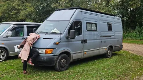 Handout A woman in a long pink jacket hugging the front of a blue van