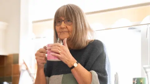 Supplied Gill Rich, a 71-year-old woman with a short white hair, leaning in front of her kitchen sink holding a mug while looking out of shot 