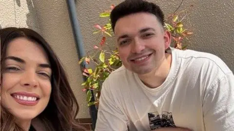 A man and woman are smiling at the camera. Both have dark hair