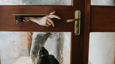 Getty Images A man reaches an arm through a letterbox towards a door handle