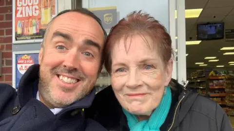 Matt Murray Matt Murray, wearing a navy blue coat and with a short trimmed beard and moustache, smiles for a selfie next to Anne Hughes, who had short red hair and a blue scarf