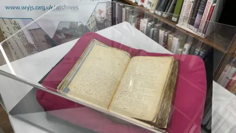 BBC/Sofia Luis-Hobbs A large old book in a display case.
