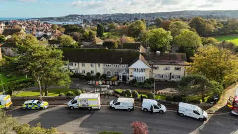 Getty Images Drone image of the two-storey, cream-coloured care home with a line of police, fire and gas vehicles parked outside. There are trees behind the building and the town of Swanage in the distance beyond.