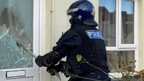 Devon and Cornwall Police A police officer smashing in a glass panel on a door