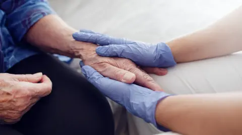 Getty Images Nurse holding elderly woman's hand.