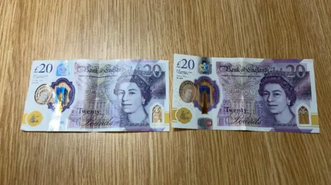 Two £20 notes are side by side, they have Queen Elizabeth the Second's face on them. They look nearly identical but the one on the right, which is real, has a slightly darker shade of purple.