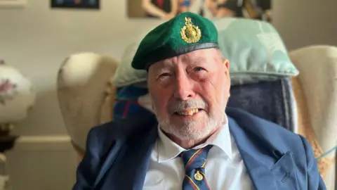 Joseph Douglas Cheshire wearing a smart suit with a tie and a green beret from his time in the Royal Marines