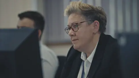 Cambridgeshire Police Det Ch Insp Helen Tebbit is looking at something to the left of the camera. She is wearing a blazer and white shirt as well as brown framed glasses. She has short blonde hair. 