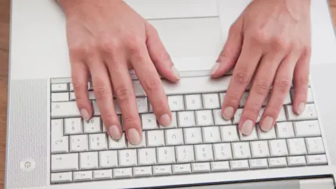 Getty Images Stock image showing a grey laptop keyboard. A woman's hands are resting on the keys as if about to type.