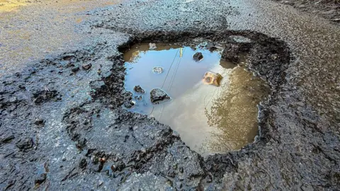 Getty Images Rain fills pot holes on a country road