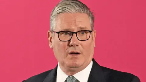 Reuters Sir Keir Starmer in front of a red background, wearing a dark suit and white shirt.