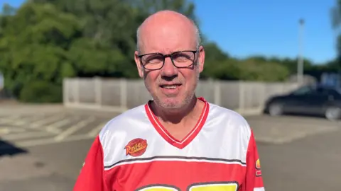 Jack Maclean/BBC Andy King, a man looking directly at the camera. He is wearing a red and white Lightning McQueen jersey.