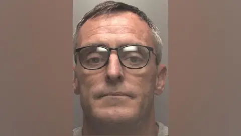 Merseyside Police Michael Hobson has short greying hair, black spectacles and is clean shaven in this custody shot.