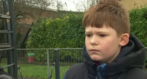 Harry looking at the camera has red hair, brown eyes and is wearing a black and blue puffer jacket.