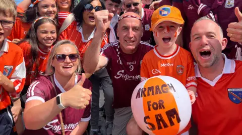 BBC Group of people in Armagh and Galway jerseys cheering. In the front a young boy holding an orange and white beach ball with 'Armagh for Sam' written on it