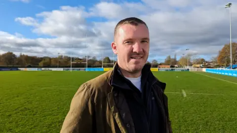 BBC Tom Foley looking at the camera standing on an empty rugby pitch
