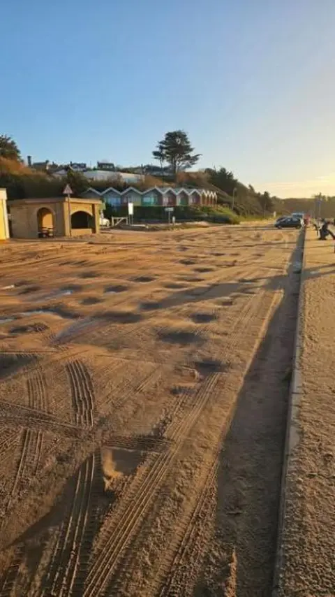 Sue Babb A seafront covered with sand and some beach huts in the distance.