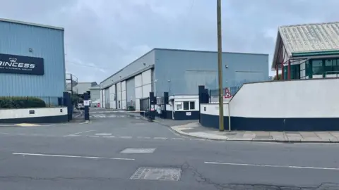 A building branded Princess can be seen to the left, with other warehouse type buildngs to the right with a road in the foreground. 