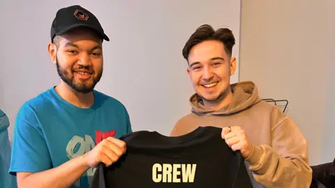 David Izekor (left) and university flatmate George Child are pictured together holding a black t-shirt that says crew