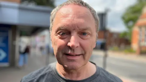 BBC John Gellard - he has short grey hair and blue eyes. He is wearing a grey T-shirt and is looking directly at the camera.
