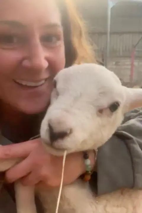 Charlie Lillington Close up photo of Charlie Lillington holding a lamb and smiling at the camera