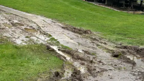 Supplied A muddy pathway on which the grass and soil appears to have been pulled up and disrupted by car tyres