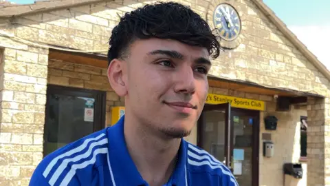 Sam Rieger sits outside a sports club in a blue adidas polo shirt.