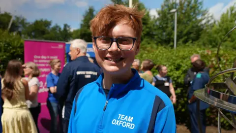 Jack Beever has short ginger hair and glasses. He is wearing a blue tracksuit top.