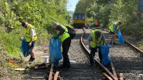 Volunteers in hi-vis vest litter pick along a railway track 