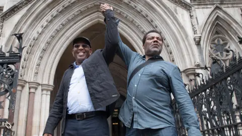 Paul Green (left) and Cleveland Davidson hold their linked hands aloft outside the entrance to the Royal Courts of Justice