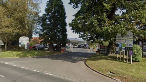 The entrance to the Garden Centre, with large trees framing the driveway into it. The signs either side it read 'Bell Plantation' 