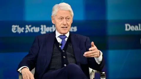 Bill Clinton gesturing while sitting in a chair during a lecture